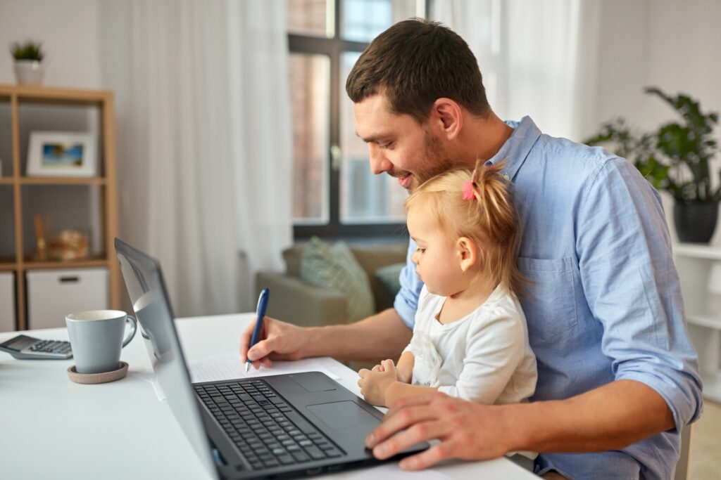 Dad at home working on computer with young daughter on basic life insurance